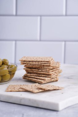 Sağlıklı çıtır çıtır krakerler, susam tohumları ve mermer tahtada yeşil zeytinler.