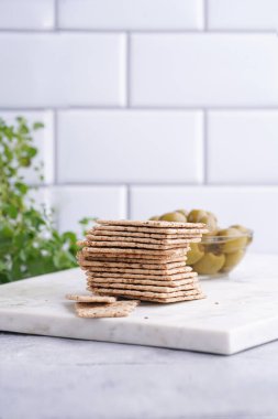 Sağlıklı çıtır çıtır krakerler, susam tohumları ve mermer tahtada yeşil zeytinler.