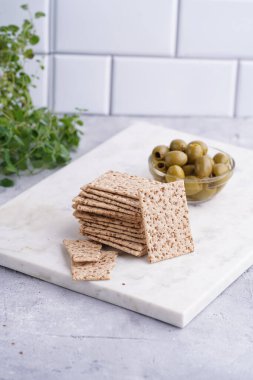 Sağlıklı çıtır çıtır krakerler, susam tohumları ve mermer tahtada yeşil zeytinler.