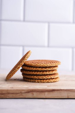 Stroopwafel - geleneksel Hollanda usulü karamelli gözleme - tahta bir tahtanın üzerinde üst üste istiflenmiş, beyaz mutfak. Kapat.