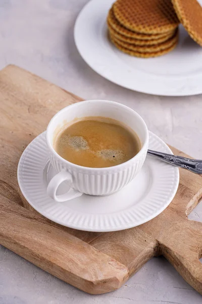 Stroopwafel - geleneksel Hollanda usulü karamelli gözleme - tahtanın üzerinde üst üste istiflenmiş beyaz mutfak ve beyaz porselen fincanda bir fincan kahve