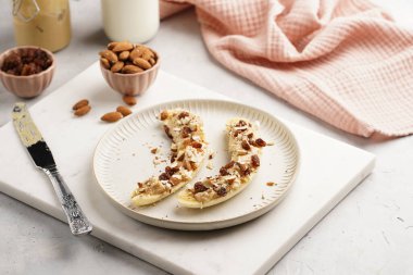 Fıstık ezmesi, kuru üzüm, badem ve beyaz tabakta chia tohumlarıyla hazır iki muz.