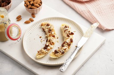 Fıstık ezmesi, kuru üzüm, badem ve beyaz tabakta chia tohumlarıyla hazır iki muz.