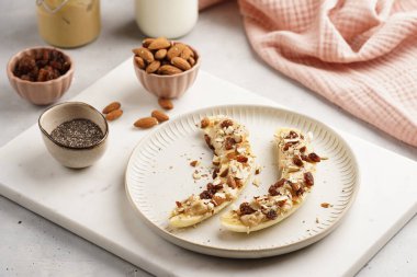 Fıstık ezmesi, kuru üzüm, badem ve beyaz tabakta chia tohumlarıyla hazır iki muz.