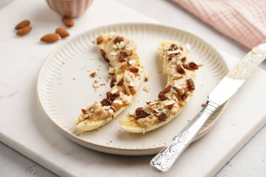 Fıstık ezmesi, kuru üzüm, badem ve beyaz tabakta chia tohumlarıyla hazır iki muz.