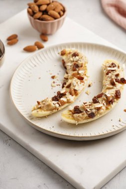 Fıstık ezmesi, kuru üzüm, badem ve beyaz tabakta chia tohumlarıyla hazır iki muz.