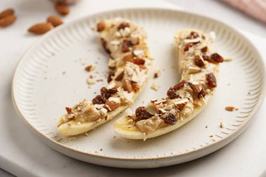 Fıstık ezmesi, kuru üzüm, badem ve beyaz tabakta chia tohumlarıyla hazır iki muz.