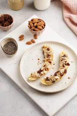 Fıstık ezmesi, kuru üzüm, badem ve beyaz tabakta chia tohumlarıyla hazır iki muz.