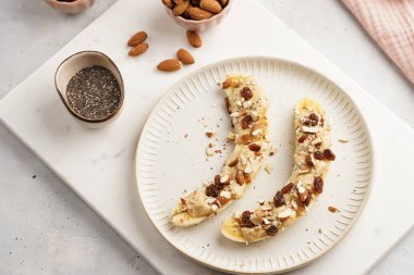 Fıstık ezmesi, kuru üzüm, badem ve beyaz tabakta chia tohumlarıyla hazır iki muz.