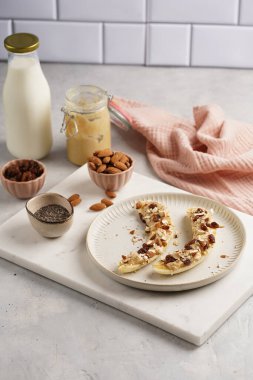 Fıstık ezmesi, kuru üzüm, badem ve beyaz tabakta chia tohumlarıyla hazır iki muz.