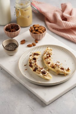 Fıstık ezmesi, kuru üzüm, badem ve beyaz tabakta chia tohumlarıyla hazır iki muz.