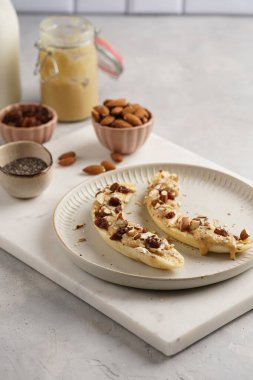 Fıstık ezmesi, kuru üzüm, badem ve beyaz tabakta chia tohumlarıyla hazır iki muz.