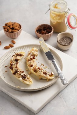 Fıstık ezmesi, kuru üzüm, badem ve beyaz tabakta chia tohumlarıyla hazır iki muz.