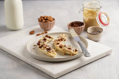 Fıstık ezmesi, kuru üzüm, badem ve beyaz tabakta chia tohumlarıyla hazır iki muz.