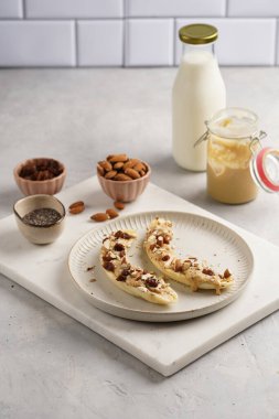 Fıstık ezmesi, kuru üzüm, badem ve beyaz tabakta chia tohumlarıyla hazır iki muz.