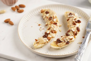 Fıstık ezmesi, kuru üzüm, badem ve beyaz tabakta chia tohumlarıyla hazır iki muz.