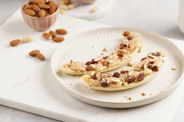 Fıstık ezmesi, kuru üzüm, badem ve beyaz tabakta chia tohumlarıyla hazır iki muz.