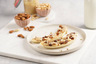 Fıstık ezmesi, kuru üzüm, badem ve beyaz tabakta chia tohumlarıyla hazır iki muz.