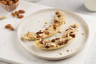 Fıstık ezmesi, kuru üzüm, badem ve beyaz tabakta chia tohumlarıyla hazır iki muz.