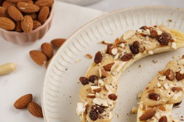 Fıstık ezmesi, kuru üzüm, badem ve beyaz tabakta chia tohumlarıyla hazır iki muz.
