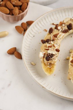 Fıstık ezmesi, kuru üzüm, badem ve beyaz tabakta chia tohumlarıyla hazır iki muz.