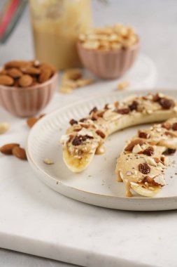 Fıstık ezmesi, kuru üzüm, badem ve beyaz tabakta chia tohumlarıyla hazır iki muz.