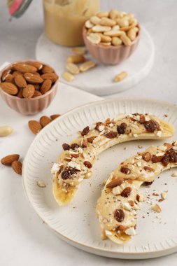 Fıstık ezmesi, kuru üzüm, badem ve beyaz tabakta chia tohumlarıyla hazır iki muz.