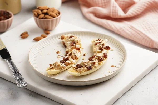 Fıstık ezmesi, kuru üzüm, badem ve beyaz tabakta chia tohumlarıyla hazır iki muz.