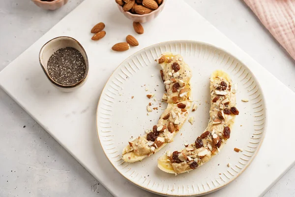 Fıstık ezmesi, kuru üzüm, badem ve beyaz tabakta chia tohumlarıyla hazır iki muz.