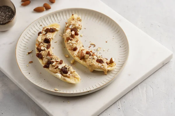 Fıstık ezmesi, kuru üzüm, badem ve beyaz tabakta chia tohumlarıyla hazır iki muz.