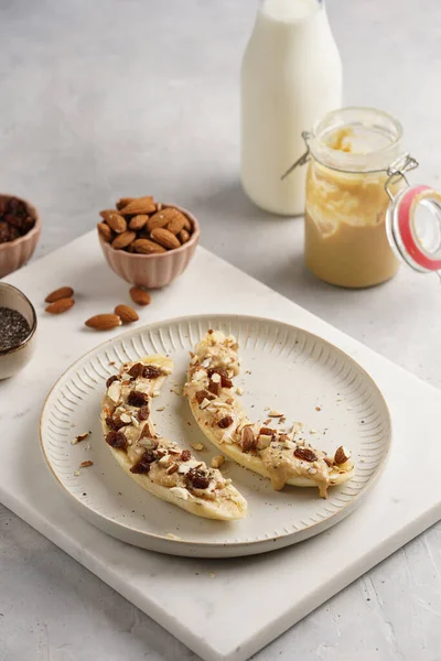 Fıstık ezmesi, kuru üzüm, badem ve beyaz tabakta chia tohumlarıyla hazır iki muz.