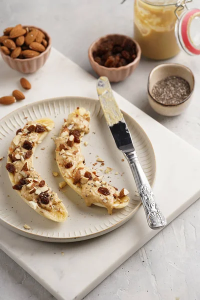 Fıstık ezmesi, kuru üzüm, badem ve beyaz tabakta chia tohumlarıyla hazır iki muz.