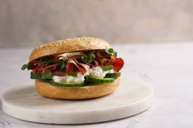 Pastırmalı simit sandviç, salatalık dilimleri, su teresi salatası ve mermer zemin üzerinde ricotta.