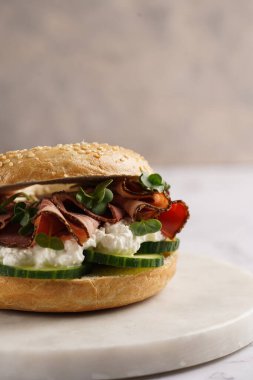 Pastırmalı simit sandviç, salatalık dilimleri, su teresi salatası ve mermer zemin üzerinde ricotta.