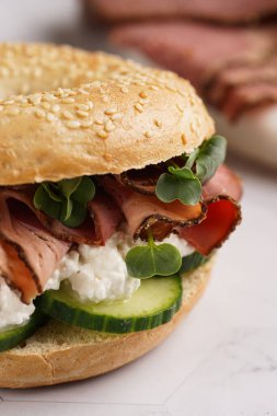 Pastırmalı simit sandviç, salatalık dilimleri, su teresi salatası ve mermer zemin üzerinde ricotta.