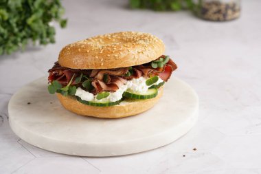 Pastırmalı simit sandviç, salatalık dilimleri, su teresi salatası ve mermer zemin üzerinde ricotta.