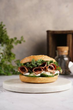 Pastırmalı simit sandviç, salatalık dilimleri, su teresi salatası ve mermer zemin üzerinde ricotta.