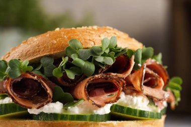 Pastırmalı simit sandviç, salatalık dilimleri, su teresi salatası ve mermer arka planda ricotta, yakın plan, seçici odak