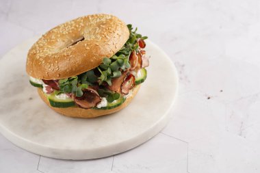 Pastırmalı simit sandviç, salatalık dilimleri, su teresi salatası ve mermer tahtada ricotta.