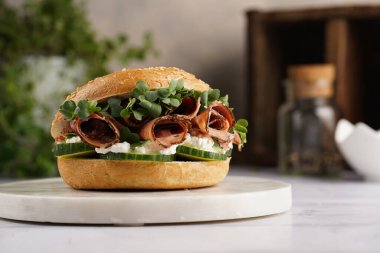 Pastırmalı simit sandviç, salatalık dilimleri, su teresi salatası ve mermer tahtada ricotta.