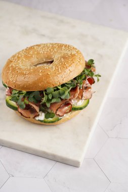 Pastırmalı simit sandviç, salatalık dilimleri, su teresi salatası ve mermer tahtada ricotta.