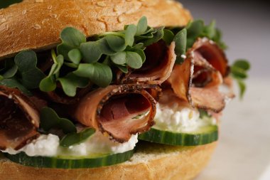 Pastırmalı simit sandviç, salatalık dilimleri, su teresi salatası ve mermer tahtada ricotta, yakın plan, seçici odaklanma.