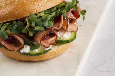 Pastırmalı simit sandviç, salatalık dilimleri, su teresi salatası ve mermer tahtada ricotta, yakın plan, seçici odaklanma.