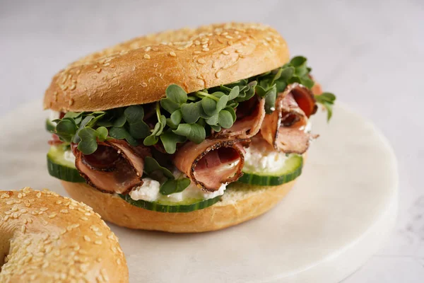 Pastırmalı simit sandviç, salatalık dilimleri, su teresi salatası ve mermer tahtada ricotta.