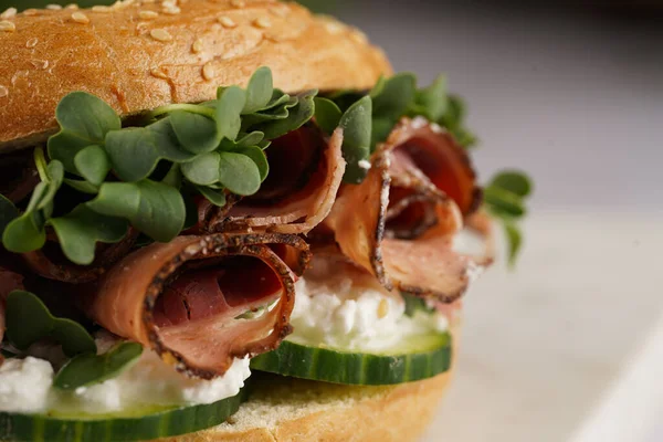 Pastırmalı simit sandviç, salatalık dilimleri, su teresi salatası ve mermer tahtada ricotta, yakın plan, seçici odaklanma.