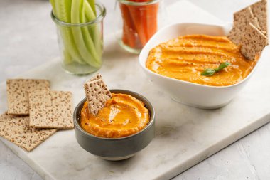 Kırmızı biber sosu portakallı kabak püresi gibi görünüyor, susam tohumlu ince krakerler, uzun şeritler ve mermer tahta üzerinde çubuklarla kesilmiş havuç ve salatalık.