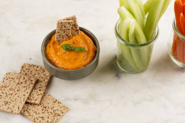 Kırmızı biber sosu portakallı kabak püresi gibi görünüyor, susam tohumlu ince krakerler, uzun şeritler ve mermer tahta üzerinde çubuklarla kesilmiş havuç ve salatalık.