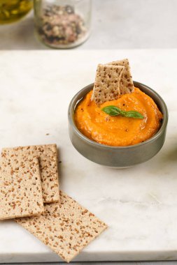 Kırmızı biber sosu portakallı kabak püresi gibi görünüyor, susam tohumlu ince krakerler, uzun şeritler ve mermer tahta üzerinde çubuklarla kesilmiş havuç ve salatalık.
