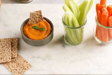 Kırmızı biber sosu portakallı kabak püresi gibi görünüyor, susam tohumlu ince krakerler, uzun şeritler ve mermer tahta üzerinde çubuklarla kesilmiş havuç ve salatalık.