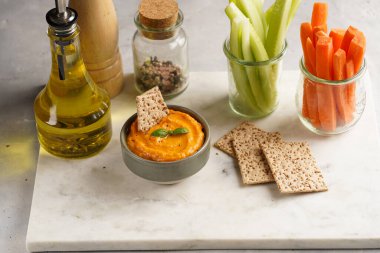 Kırmızı biber sosu portakallı kabak püresi gibi görünüyor, susam tohumlu ince krakerler, uzun şeritler ve mermer tahta üzerinde çubuklarla kesilmiş havuç ve salatalık.